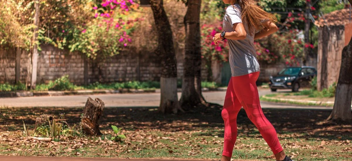 A woman jogs on a path surrounded by trees and vibrant flowers, embodying a healthy lifestyle.
