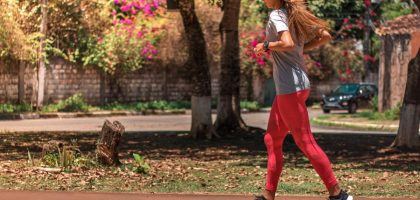 A woman jogs on a path surrounded by trees and vibrant flowers, embodying a healthy lifestyle.