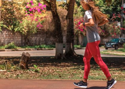 A woman jogs on a path surrounded by trees and vibrant flowers, embodying a healthy lifestyle.